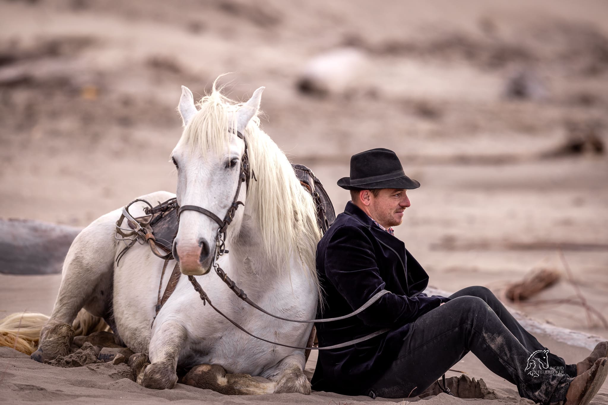 Hirte sitzt bei seinem Camarguepferd im Sand